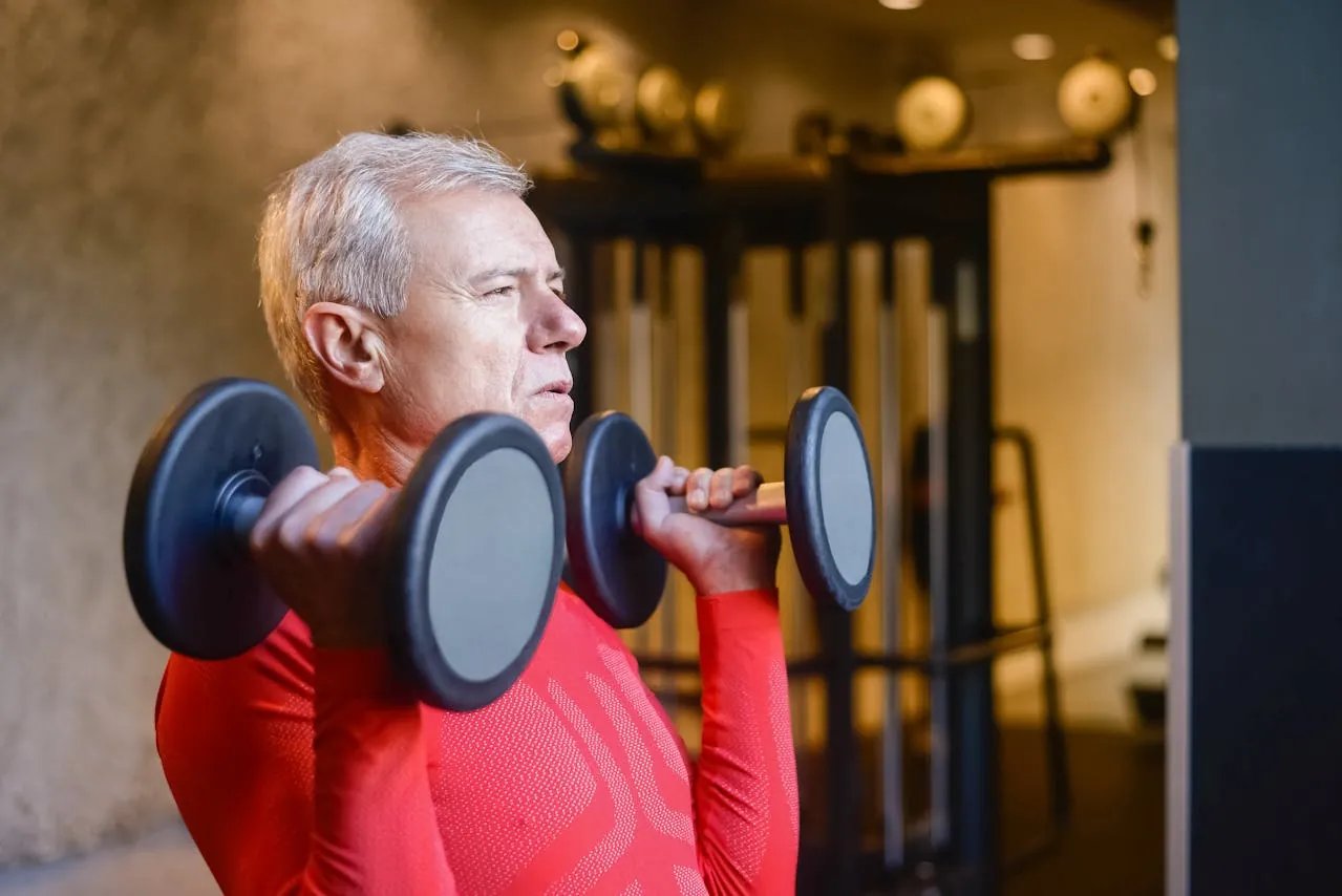 Older man doing a dumbbell shoulder press in a gym